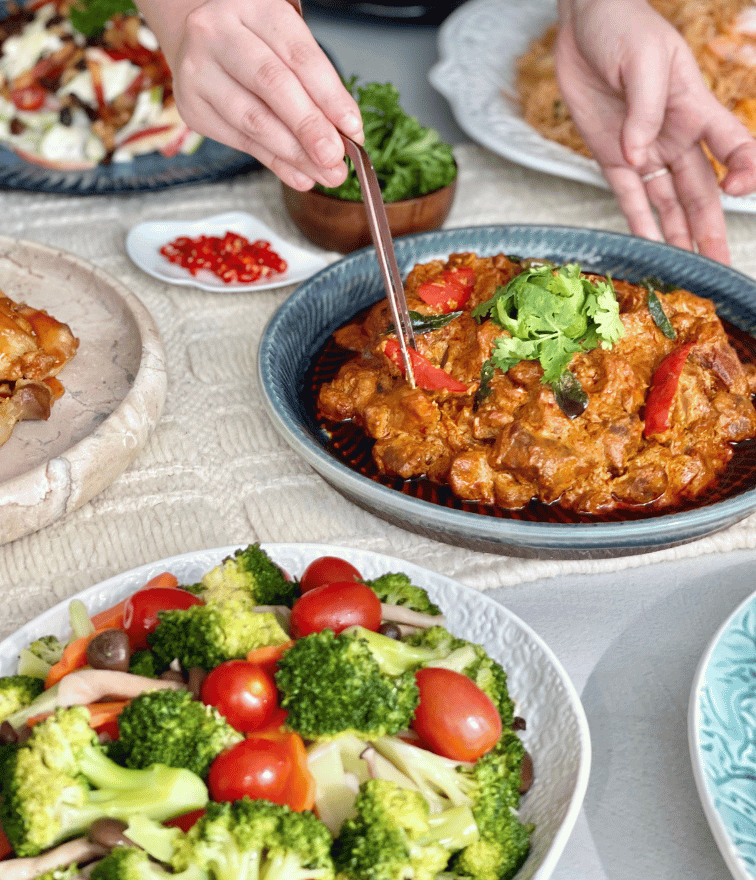 Assortment vegetables with broccoli and tomatoes, hands using chopstick to get spicy chicken dish