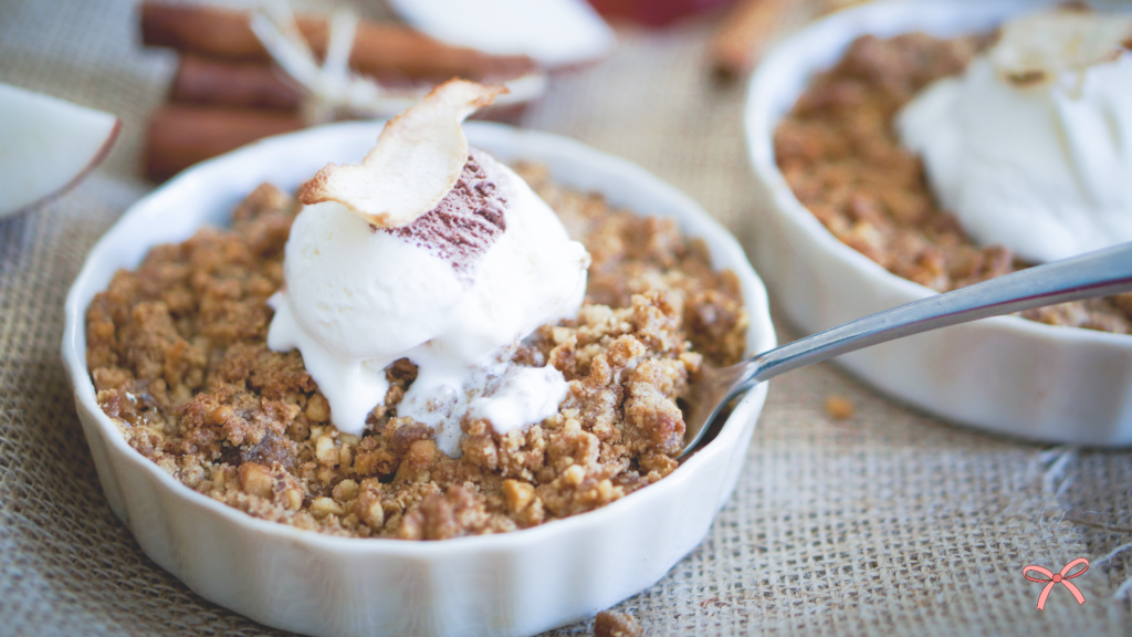 A small dish of apple crumble topped with a scoop of vanilla ice cream.